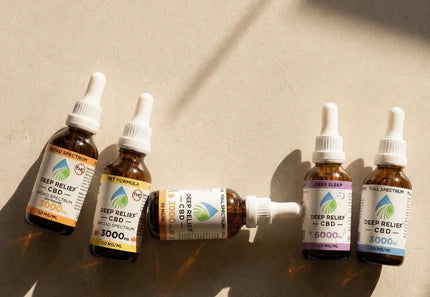Five amber CBD tincture dropper bottles on a beige surface with strong sunlight and shadows.